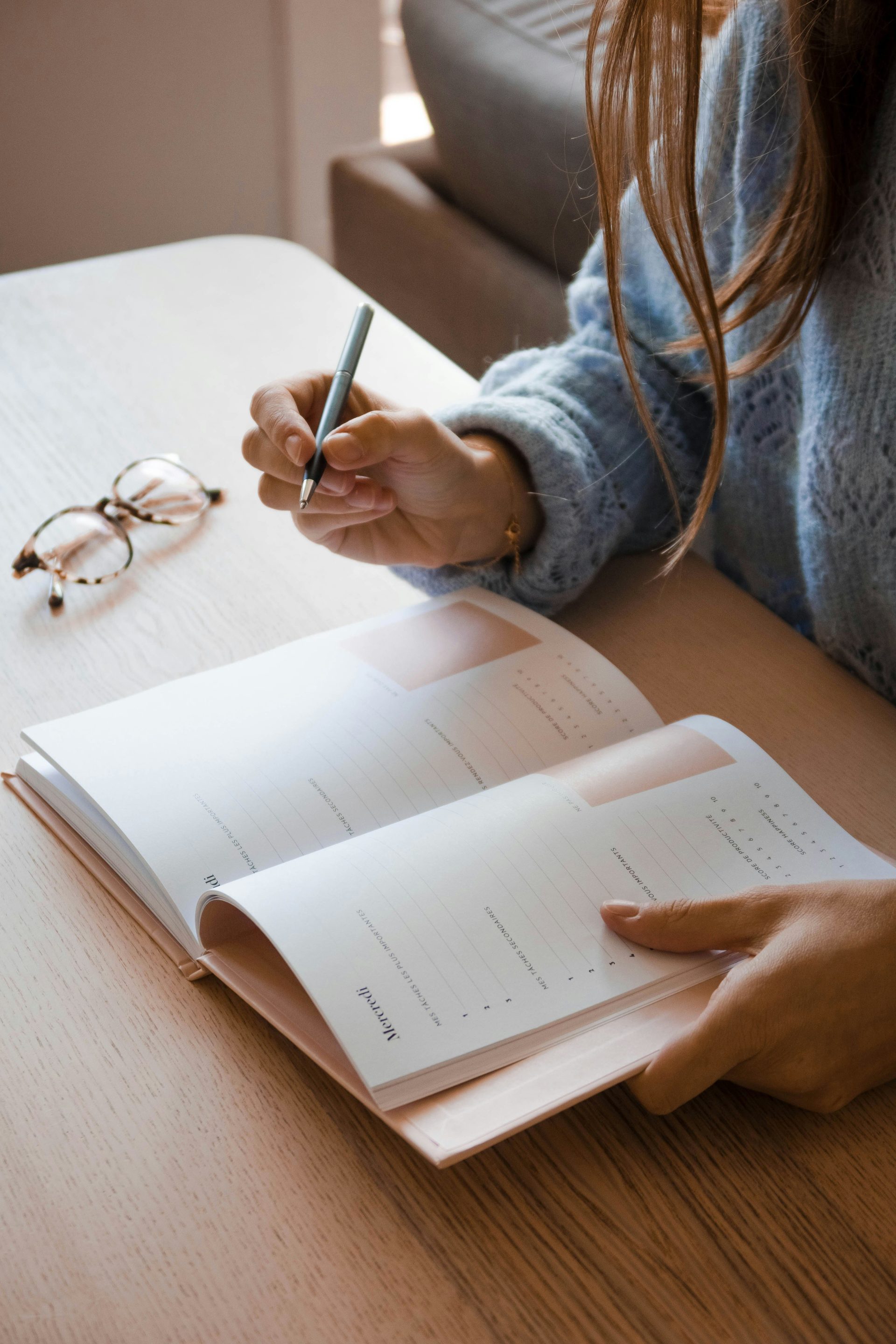 Frau in weißem Langarmshirt hält einen Stift und schreibt auf weißes Papier.